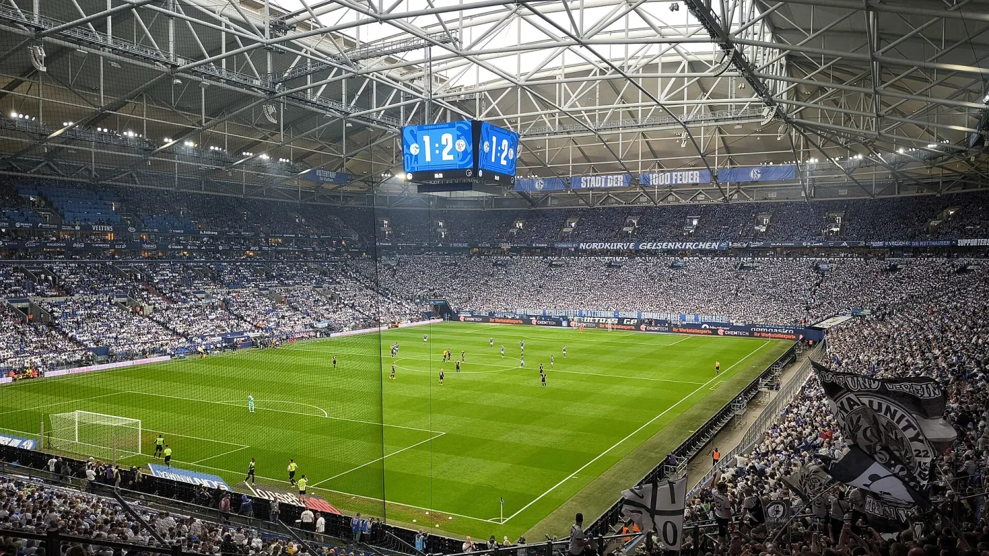 A full stadium under a closed roof, seen from the upper tier, with play under way on the pitch below.